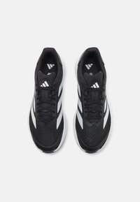 Une paire de chaussures de course Adidas noires et blanches avec des tiges en maille, des lacets et les trois bandes emblématiques vues de dessus sur un fond blanc.
