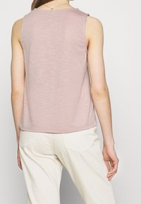 Rosa ärmlös topp med mjuk textur, rundad halsringning och subtilt slub-mönster, matchad med ljusfärgade, avslappnade byxor.