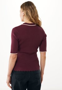 Burgundská krátká rukávová halenka z ribu s krémovými akcenty a vlnitým lemem. Navržena pro těsný siluetu.