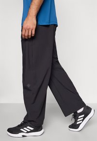 Čierne atletické nohavice s voľným strihom, hladkou tkaninou a bočnými vreckami, skombinované s čierno-bielymi teniskami s povrchom z mrežoviny a gumovou podrážkou.