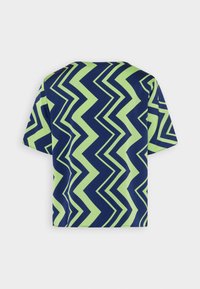 Camicia a maniche corte con un audace motivo a zigzag in blu navy e verde brillante, mostrata da dietro su uno sfondo semplice.