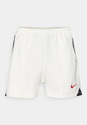 Bjele sportske kratke hlače s crnim bočnim naglascima, elastičnom strukom i crvenim Nike logom na donjoj prednjoj strani. Glatka, lagana tkanina.