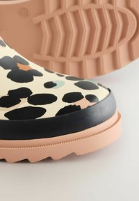 Bottines imperméables à motif léopard avec une finition brillante, des bordures noires et une semelle texturée rose. Gros plan sur le détail des orteils et de la semelle.