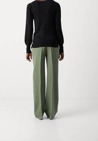 Maglione nero lavorato a maglia con maniche lunghe a sbuffo abbinato a pantaloni a vita alta e gamba larga in tessuto verde chiaro. Texture liscia, vestibilità morbida.