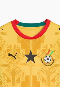Maillot de football jaune avec col rouge, étoile noire au centre, logo Puma à gauche et emblème de la Fédération ghanéenne de football à droite.