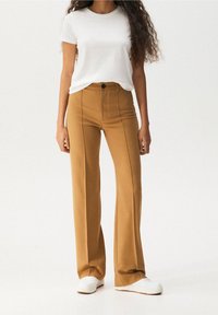 Brązowe, szerokie spodnie z wysokim pasem, przednimi kieszeniami i pionowymi przeszyciami, zestawione z prostym białym t-shirtem z okrągłym dekoltem.
