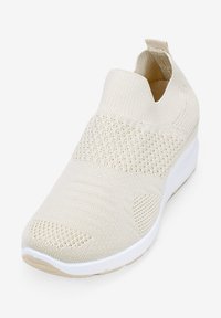 Chausson en tricot beige, à enfiler, avec une tige texturée, un col semblable à une chaussette et une semelle en caoutchouc blanc. Comprend de petites perforations pour la respirabilité.