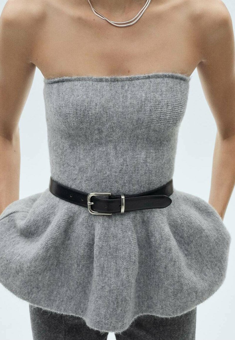 Top gris en maille sans bretelles avec taille peplum évasée, ceinture noire avec boucle argentée, porté avec un pantalon gris foncé et un collier chaîne argenté.