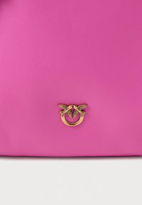 Bolsa de pele rosa com detalhes em metal dourado, com dois pássaros, logótipo em relevo e uma textura suave.