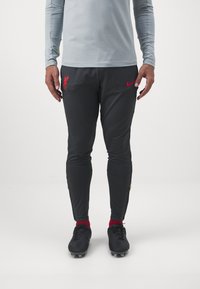 Botas de fútbol negras de Nike, pantalones ajustados grises con logotipo rojo de Liverpool y camiseta de manga larga gris claro. Tejido suave y diseño atlético.