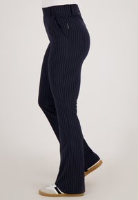 Slim-fit marineblauwe broek met streepjes en voorzakken, gedragen met witte sneakers met zwarte strepen en rubberen zolen.