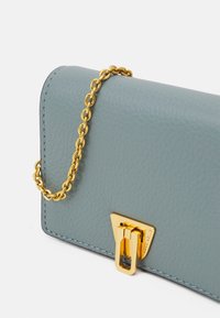 Tyrkysová kožená peněženka s texturovaným povrchem, s zlatým řetízkovým páskem a zlatým trojúhelníkovým uzávěrem.