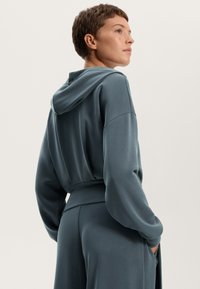 Felpa con cappuccio in verde teal smorzato, con maniche lunghe, vestibilità rilassata e tasche laterali, dal tessuto liscio e morbido.