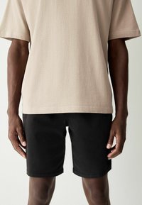 Camicetta beige a maniche corte con una finitura testurizzata abbinata a pantaloni corti neri. I pantaloni corti hanno un taglio dritto e dei risvolti.