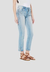 Lichtblauwe denim jeans met een aangesloten model, versierd met kralenbloemmotieven aan de linkerkant, en enkellang met een rafelige zoom.