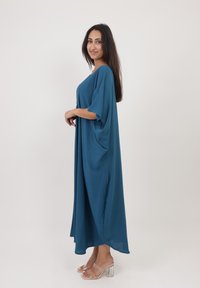 Une robe teal, ample, en tissu léger avec des manches larges, atteignant les chevilles, présentant une texture lisse et un design fluide.