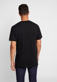 T-shirt noir à manches courtes en coton, avec un col rond et une coupe décontractée. Texture lisse sans motifs ni graphiques visibles.