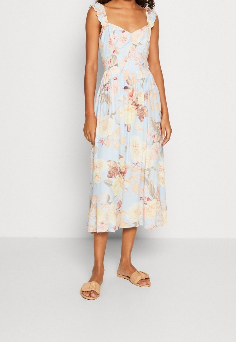 Květinové midi šaty ve světle modré barvě s volánkovými ramínky. Mají pastelové květinové vzory a stáhnutý pas. Vynikají s tělovými sandály.