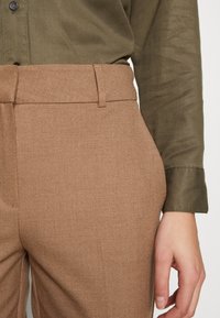 Brown tailored trousers made of textured fabric with a smooth waistband. The outfit is paired with a green shirt, featuring button closure.