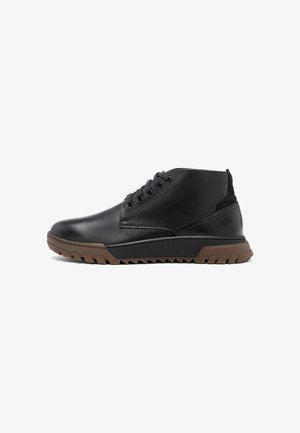 Bottes à chevilles en cuir noir avec un bout rond, une tige texturée, six œillets et une semelle en caoutchouc brun dotée de profondes rainures pour l'adhérence.