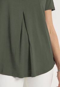 Mørkegrøn kortærmet top med en plissering foran, lavet af blødt stof, med en afslappet pasform og buet kant.