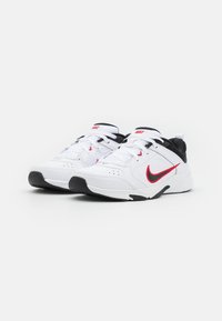 White athletic shoes with black accents and red Nike swoosh. Features a textured surface, lace-up design, and cushioned sole for comfort.