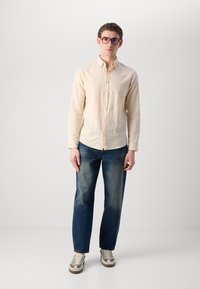 Beige linen button-up shirt, dark blue denim jeans, and gray-green sneakers with white laces. Simple design, relaxed fit, subtle textures.