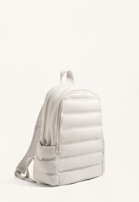 Fehér párnázott hátizsák sima, steppelt textúrával, dupla cipzárral és oldalsó zsebekkel. Minimum design, állítható vállpántokkal.