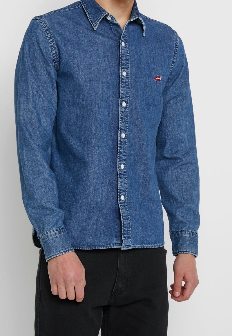 Donkerblauw denim overhemd met knoopsluiting, voorzien van een klassieke kraag, lange mouwen en een klein rood logovlekje op de linkerborst.