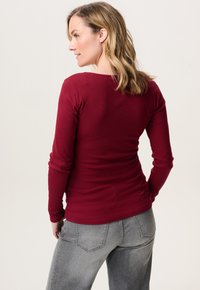 Langsleeve, getailleerde top van bordeaux ribbelstof, met een ronde hals en een zachte textuur, gecombineerd met grijze, strakke jeans.