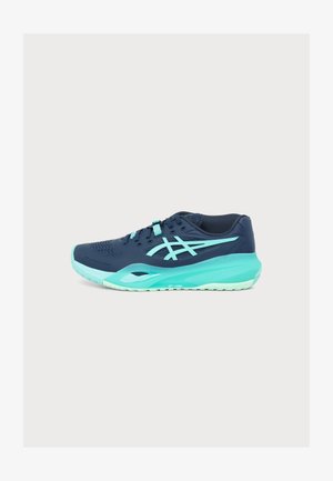 Chaussure de sport bleu marine et turquoise avec lacets et semelle rembourrée, vue de côté sur un fond clair uni.