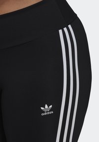 Black leggings featuring three white stripes along the side, made from a smooth, stretchy fabric, with a small white adidas logo accent.