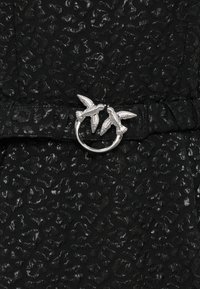 Μαύρο φόρεμα με υφή που διαθέτει μεταλλικό σχέδιο λεοπάρδαλης, με κεντημένη μέση και ασημένια κυκλική αγκράφα ζώνης διακοσμημένη με δύο φιγούρες πουλιών.