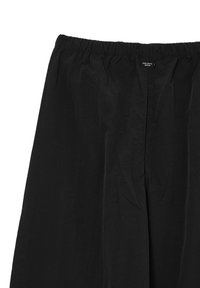 Pantalons noirs avec une taille élastique, fabriqués dans un tissu léger et texturé, présentant une coupe décontractée et un design minimaliste.