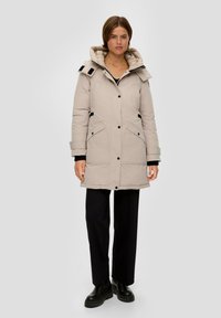Beige geïsoleerde parka met een gewatteerde capuchon, zwarte accenten, grote voorzakken en een knoopsluiting. Heeft een middellange uitstraling en een strakke textuur.