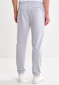 Vista posteriore di una persona che indossa pantaloni della tuta grigio chiaro con polsini elastici e una tasca posteriore, abbinati a sneaker bianche e calzini.