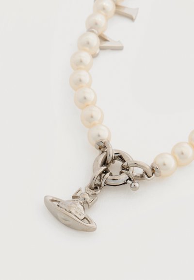 Κολιέ με πέρλες που διαθέτει γυαλιστερές λευκές πέρλες, ασημένια μεταλλικά στοιχεία με αλυσίδες συνδεδεμένες μεταξύ τους και ένα γούρι σε σχήμα πλανήτη με δαχτυλίδια.