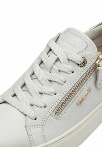 Sneaker bianca in pelle con superficie testurizzata, dotata di lacci bianchi piatti, una cerniera laterale e un accento in hardware dorato. Logo impresso sul lato.