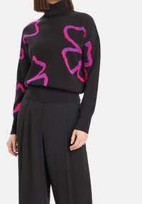 Svart stickad tröja med hög krage, prydd med stora, strukturerade rosa och blå abstrakta former. Mjuk tyg med långa ärmar och en avslappnad passform.