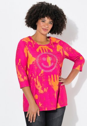 Różowo-pomarańczowa koszula tie-dye z rękawami o długości trzech kwart i zdesignowaną na przodzie twarzą uśmiechniętą z dżetami. Miękki, casualowy materiał.