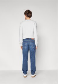 Maglione grigio chiaro a maniche lunghe, abbinato a jeans in denim blu. I jeans presentano doppie tasche posteriori e un'etichetta sul cinturino.