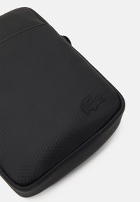 Borsa nera con zip realizzata in materiale testurizzato. Presenta un logo in rilievo sulla parte anteriore e una forma curvata e imbottita per una maggiore protezione.