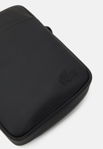 Pochette zippée noire en matériau texturé. Elle présente un logo en relief sur le devant et une forme courbée et rembourrée pour une protection accrue.