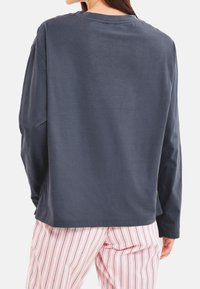 Tummaharmaa pitkähihaisen paidan, jossa on rento malli, pyöreä kaula-aukko ja sileä texture, yhdistetty vaaleanpunaisiin raidoitettuihin pyjamas-housuihin.