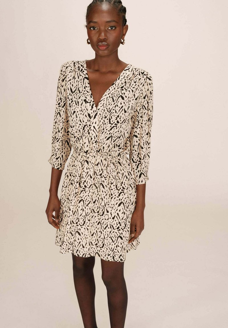 Robe à manches courtes avec un décolleté en V, présentant un motif abstrait noir et blanc, une taille cintrée et une jupe fluide arrivant au genou.