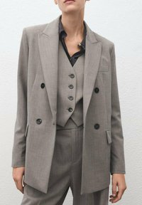 Traje de tres piezas gris con rayas, que incluye un blazer de doble botonadura, chaleco con botones y pantalones a medida. Tejido texturizado.