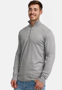 Suéter gris con cremallera y mangas largas, hecho de una tela suave, que presenta un cuello alto y puños acanalados. Diseño sencillo y aerodinámico sin patrones.