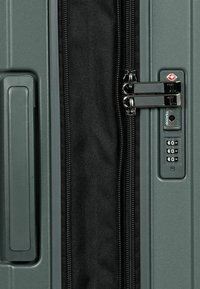 Dunkelgrüner Hartschalenkoffer mit einem schwarzen Reißverschluss, TSA-Schloss und einem Zahlenkombinationsschloss. Seitengriff ist sichtbar. Texturierte Oberfläche.