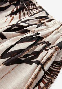 Jupe à taille élastique en tissu beige avec un motif de feuilles tropicales noir et marron. Présente une texture froncée et un design fluide.