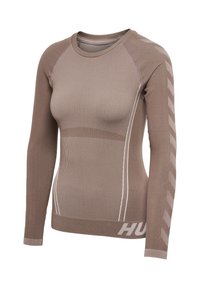 Haut d'entraînement beige ajusté à manches longues avec texture côtelée, motif chevron sur les manches et texte partiel "HUM" près de l'ourlet.